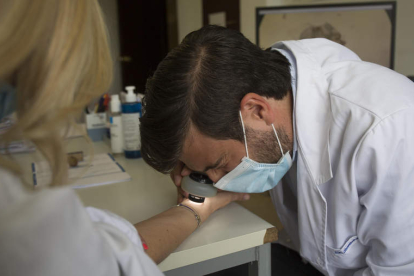 El dermatólogo José Castiñeiras González observa con una lupa la lesión en la piel para confirmar la sarna. FERNANDO OTERO
