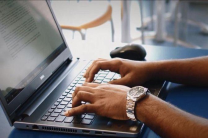 Un hombre teclea en un ordenador portátil.