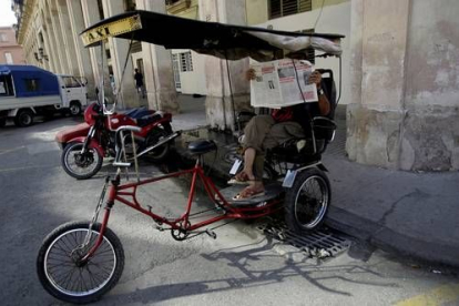 Las bicicletas son un socorrido recurso en toda la isla y un tesoro para sus propietarios. En este caso, la bici es también una forma de vida para este taxista que traslada a sus viajeros en un triciclo. Mientras llegan, el conductor se entretiene con el «Gramma», el periódico oficial del régimen, sometido también a restricciones. No resulta fácil adquirirlo.