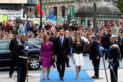 La reina y los príncipes de Asturias a su llegada al Teatro Campoamor de Oviedo. Tras ellos, la protesta por los recortes. José Luis Cereijido