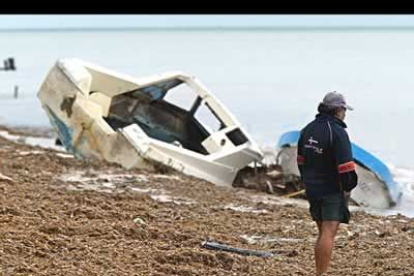 Un hombre mira una de las embarcaciones afectadas en una playa completamente cubierta por algas y materiales arrastrados por el tifón.