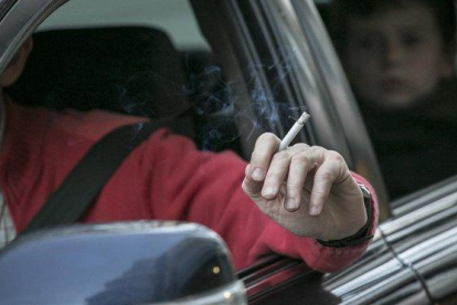 Un conductor fumando mientras conduce, con un menor detrás.
