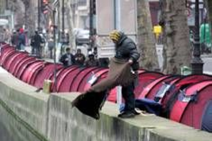 Un hombre sacude una manta a un canal de París, donde acampa gente sin hogar