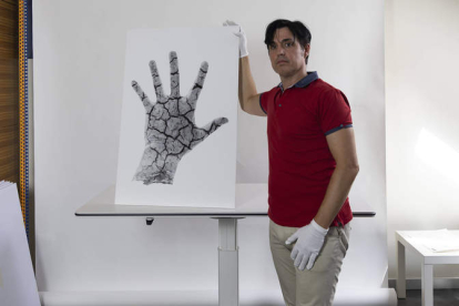 Richard Le Manz junto a una de sus obras en la que aparece la mano del artista en simbiosis con el fondo del pantano de Luna vacío durante la sequía de 2017. DL