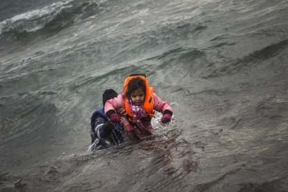 Un hombre ayuda a un niño cuyo barco ha naufragado este domingo en el Egeo.