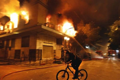 Un ciclista ante edificios incendiados en Atenas. Foto: YANNIS BEHRAKIS | REUTERS