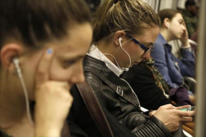 Jóvenes escuchando música con auriculares en el metro.