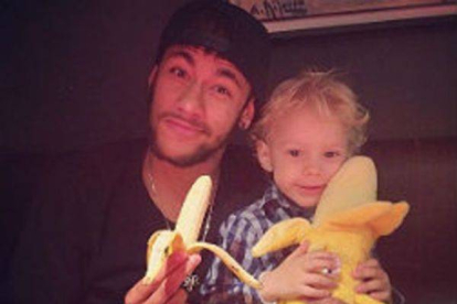 Neymar se come un plátano junto a su hijo, que sostiene un plátano de peluche.