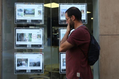 Un joven mirando ofertas de pisos de alquiler en los expositores de una inmobiliaria de Barcelona.
