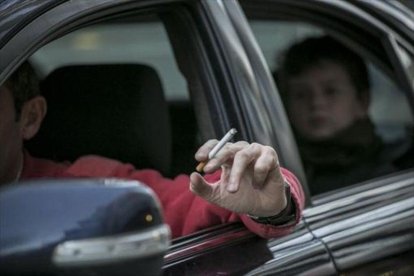 Un conductor fuma un cigarrillo en un coche, con un niño en el asiento de atrás.