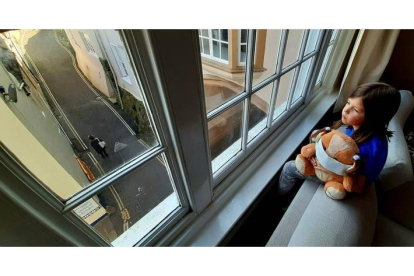 Una niña abraza a su oso de pelucho, ataviado con una máscara sanitaria, mientras miran por la ventana de su casa. ROMAN ALONSO