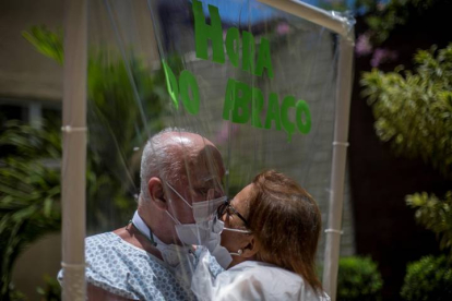 La pareja que celebrará en una semana 50 años de matrimonio, Walter Candido (paciente), de 75 años, y Marlene Amaral (visita), de 73, se besan entre una lámina plástica usada para que pacientes y familiares puedan abrazarse. ANTONIO LACERDA
