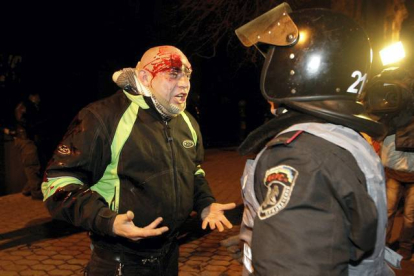 Un manifestante con una herida en la cabeza protesta frente un policía. AP / Kiev, Ucrania