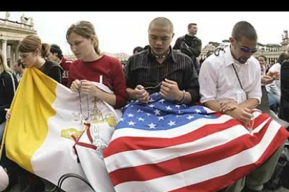 Cuatro jóvenes creyentes rezan ante una bandera del Vaticano y otra de los Estados Unidos.