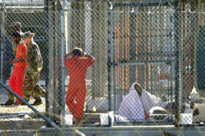 Un recluso de Guantánamo, escoltado por dos guardias en el penal, junto a otros dos presos en sus celdas, el 15 de marzo del 2002.