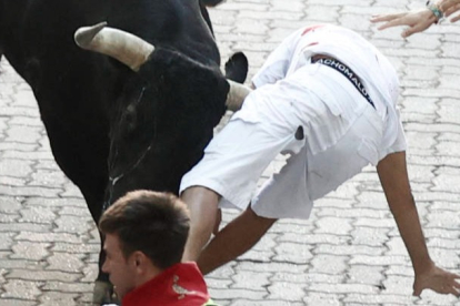 Un mozo es corneado por uno de los toros de la ganadería de Victoriano del Río durante del séptimo encierro de los sanfermines que ha durando dos minutos y 18 segundos de duración, este jueves en Pamplona. JESÚS DIGES