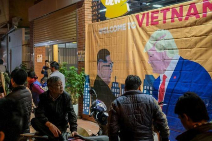 Ciudadanos de Hanói pasan ante un cartel con las imágenes de Kim y Trump horas antes de su encuentro.