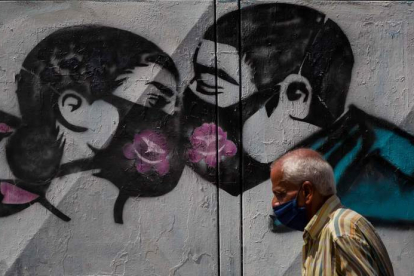 Un hombre camina frente a un grafiti que muestra una pareja besándose con mascarillas. MIGUEL GUTIERREZ