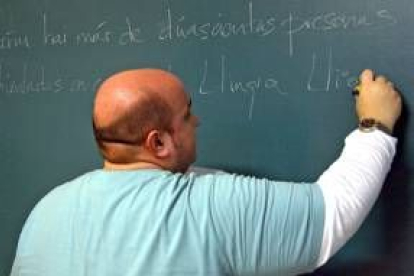 Un profesor de lengua leonesa escribe en la pizarra en una de sus clases