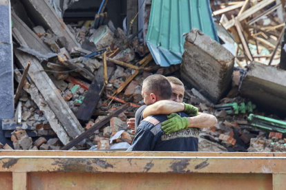 Dos bomberos se abrazan tras recoger los restos de civiles tras un bombardeo.  SERGEY KOZLOV