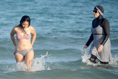 Una mujer con biquini y otra con 'burkini' en la playa tunecina de Ghar El Melh.