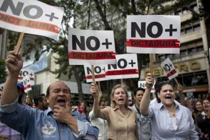 Manifestantes contrarios a Maduro sostienen pancartas en las que reclaman que se acabe la dictadura en Venezuela.