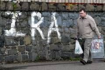 Un hombre camina ante un grafitti del IRA en el oeste de Belfast