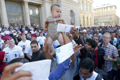Un inmigrante sirio levanta a su hijo ante la policía húngara para pedir que reabran la estación de trenes de Keleti mientras otros muestran sus billetes.