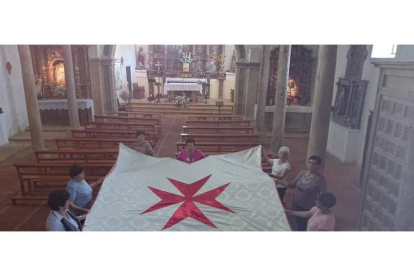 Varias vecinas de Valdavida sostienen el pendón blanco de la Orden de Malta que han podido reconstruir con una subvención del ILC.