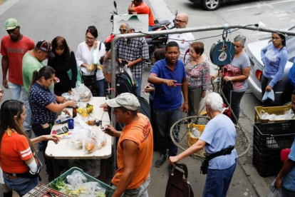 Venezolanos hacen cola para pagar la fruta y las verduras en un mercado callejero, en Caracas, el 13 de noviembre.