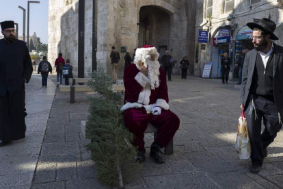 Un judíos ultraortodoxo observa con descontento a un palestino disfrazado de Papá Noel que reparte árboles.