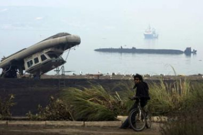 Un hombre descansa junto a un barco volcado.