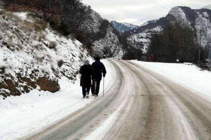 Dos ancianos caminan por una carretera nevada cerca de un pueblo de la  montaña leonesa.