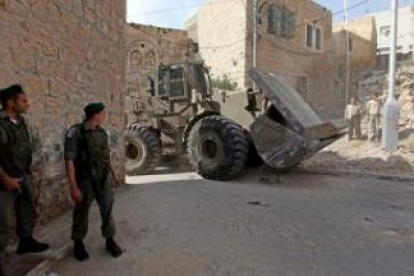 Soldados israelíes hacen guardia mientras una retroexcavadora mueve un bloque de piedra en la ciudad