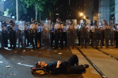 Una manifestante estirada en el suelo bloquea una de las calles de Hong Kong frente a una fila de policías.