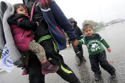 Un hombre camina llevando a dos niños bajo la lluvia junto a la frontera con Eslovenia.