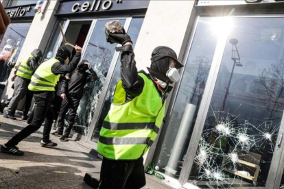 Un chaleco amarillo rompe el cristal de una tienda en los Campos Elíseos de París.