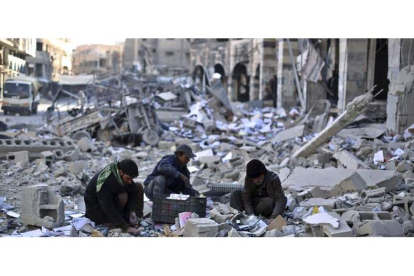 Varios hombres recogen objetos entre los escombros tras un bombardeo entre el Daesh y la coalición internacional.