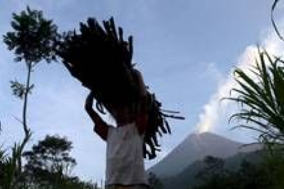 Una residente porta leña mientras el monte Merapi escupe humo y lava