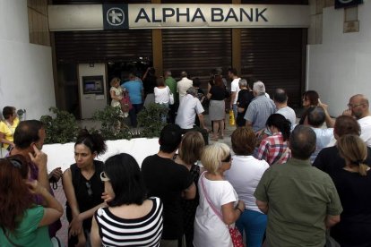 Decenas de personas hacen cola para sacar dinero de un banco en Atenas.