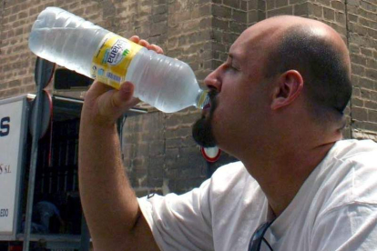 Un hombre bebe de una botella de agua mineral.