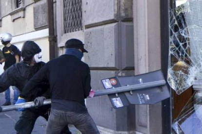 Dos encapuchados usan una señal de tráfico para romper el escaparate de un banco en el centro de Roma, Italia. Foto: EFE