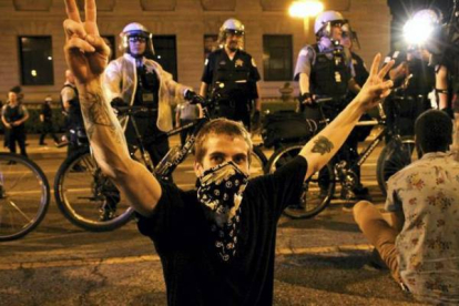 Un encapuchado sentado en el suelo con gesto de protesta ante la vigilancia de la policía de Chicago. Foto: RICARDO MIR DE FRANCIA / Chicago