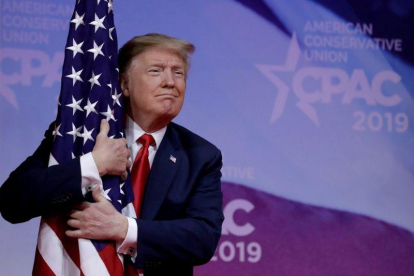 El presidente Donald Trump abrazando una bandera de su país.