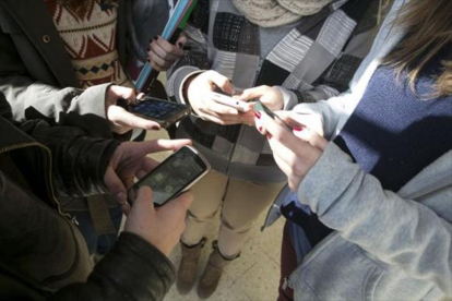 Cuatro jóvenes manipulan sus móviles.