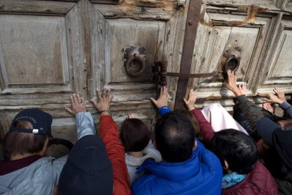 Varios peregrinos rezan y tocan la puerta del lugar del Santo Sepulcro, ayer.