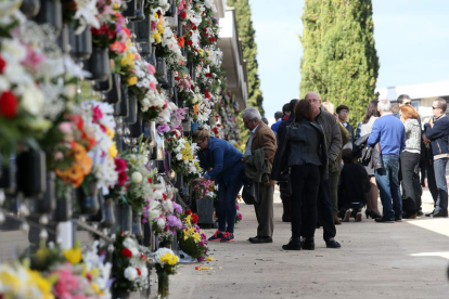 Un grupo de persona coloca flores en los jarrones de los nichos del cementerio.