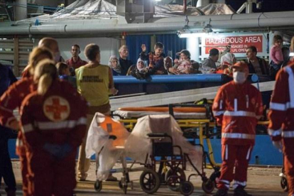 Los inmigrantes supervivientes de un naufragio llegan este jueves a tierra firme tras ser salvados por las autoridades de Libia, mientras los equipos médicos se llevan los cuerpos de los fallecidos.