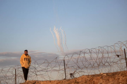 Se disparan cohetes desde la Franja de Gaza (al fondo) mientras un palestino desplazado camina cerca de la frontera palestino-egipcia en el campamento de Rafah