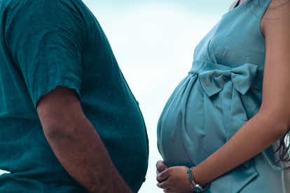 Hombre con sobrepeso y mujer embarazada, frente a frente, sosteniendo sus vientres con sus manos.